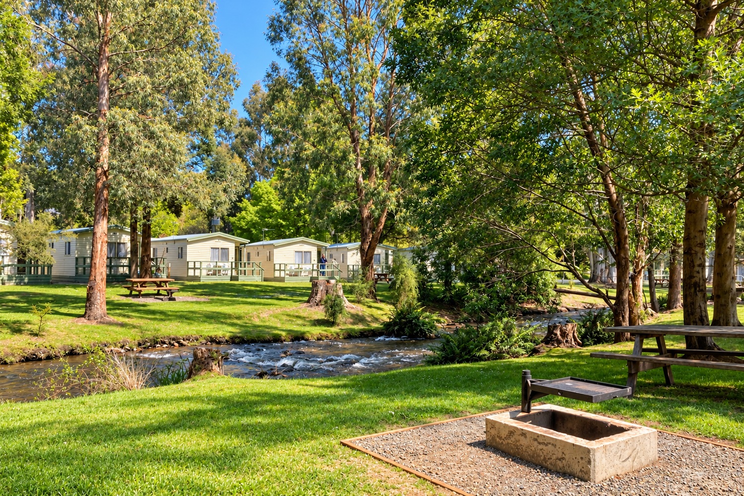 River, cabins, picnic tables and firepit at Marysville Holiday Park.