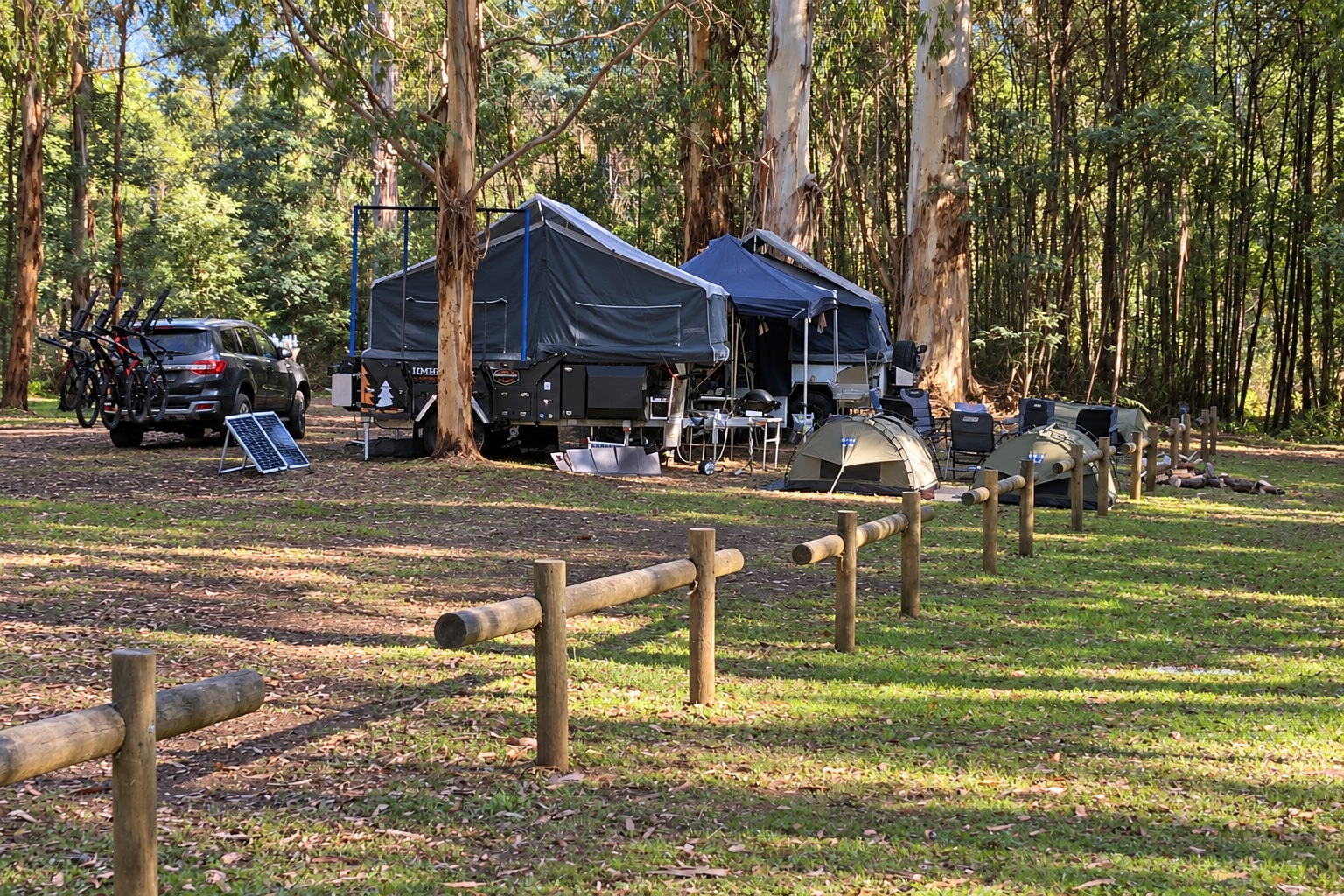 Camper trailers, tents and portable camping equipment on a wooded campsite.