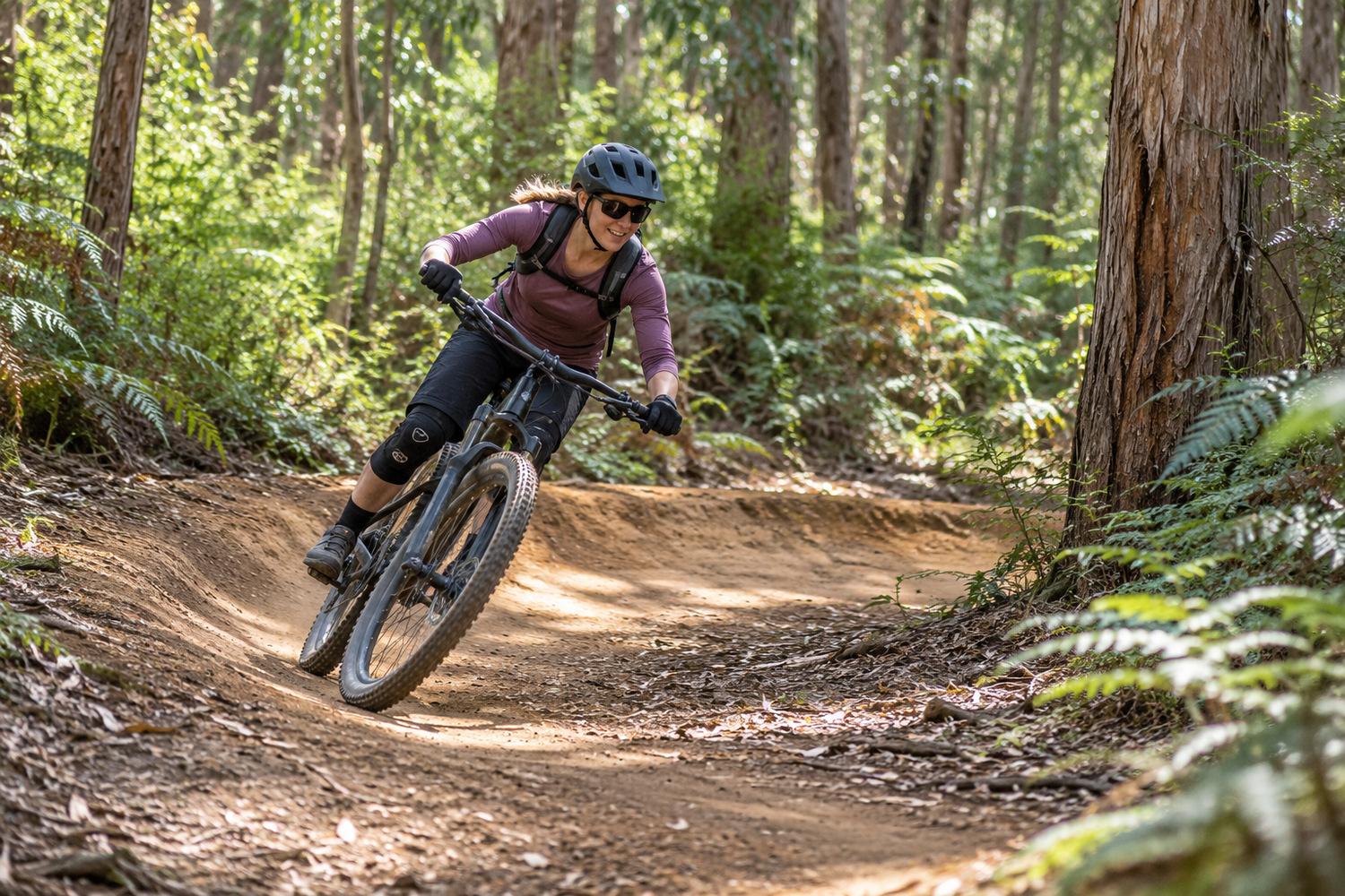 Helmeted mountain biker riding a banked dirt corner through eucalyptus forest.