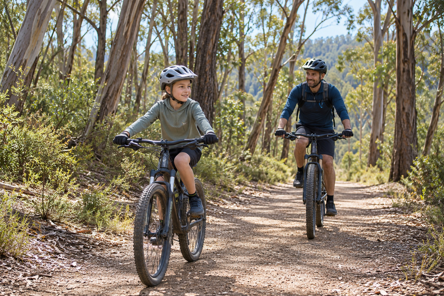 Adult and child wearing helmets while cycling along a gentle eucalyptus forest track.
