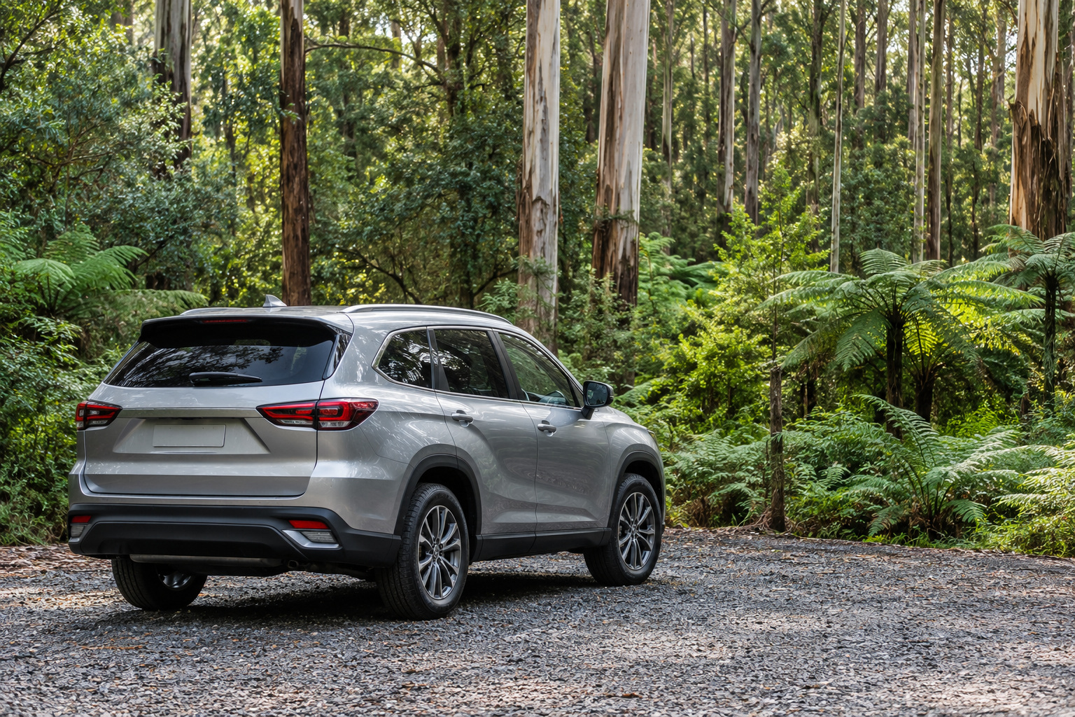 A silver SUV is parked on gravel among eucalypts and tree ferns.